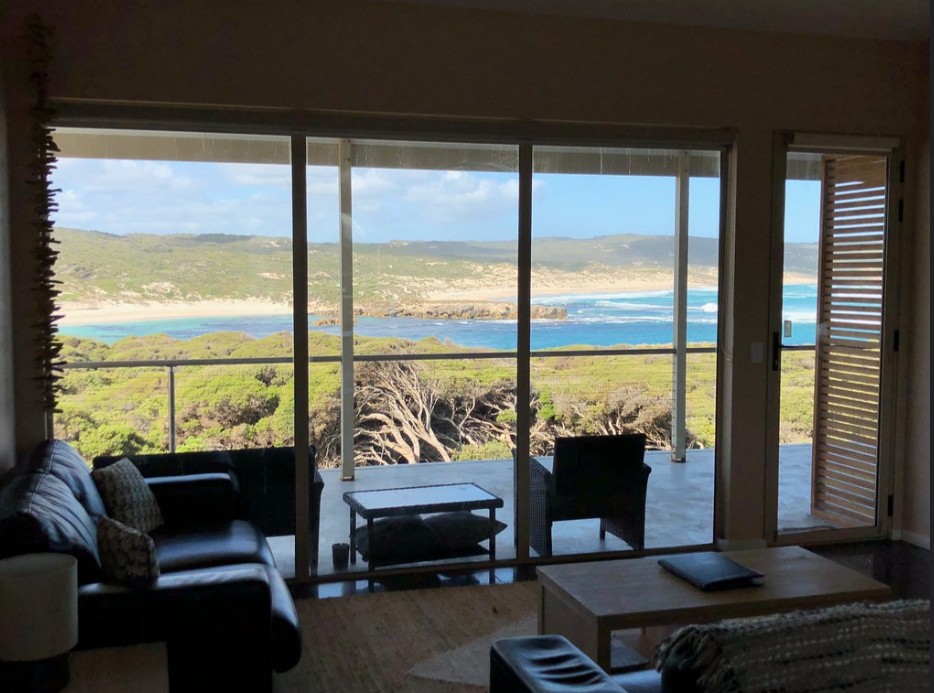 Ocean view from inside a hotel room looking through large windows and sliding doors toward the coastline