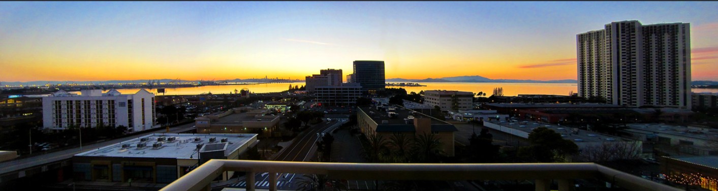 Panoramic city hotel room view at sunset with a wide skyline and water in the distance